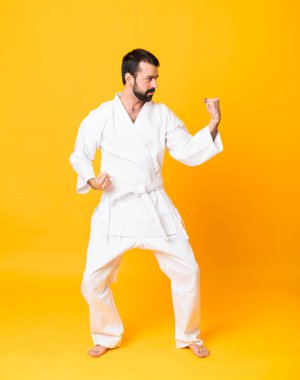 İzole edilmiş sarı arka planda karate yapan bir adamın tam boy fotoğrafı.