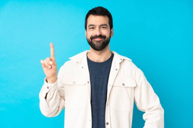 Mavi arka planda beyaz kadife ceketli genç ve yakışıklı bir adam en iyinin işareti olarak parmağını kaldırıyor.