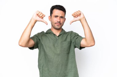 Soyutlanmış beyaz arka planda genç yakışıklı bir adam baş parmağını iki eliyle aşağı gösteriyor.