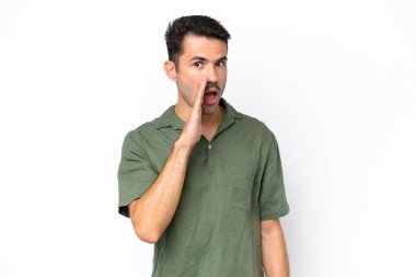 Young handsome man over isolated white background whispering something with surprise gesture while looking to the side