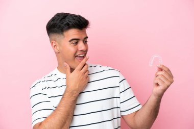 Young caucasian man holding invisaling isolated on pink background with surprise and shocked facial expression