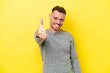 Beyaz tenli yakışıklı adam sarı arka planda izole edilmiş ve iyi bir anlaşma için el sıkışıyor.