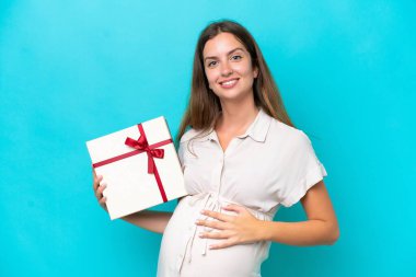 Young caucasian woman isolated on blue background pregnant and holding a gift