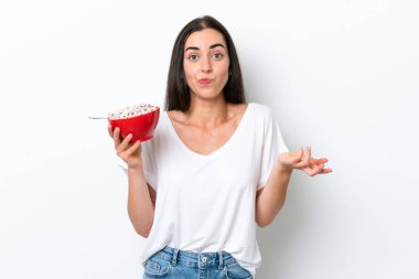 Beyaz arka planda kahvaltı sütü içen beyaz bir kadın omuzlarını kaldırırken şüpheyle hareket ediyor.