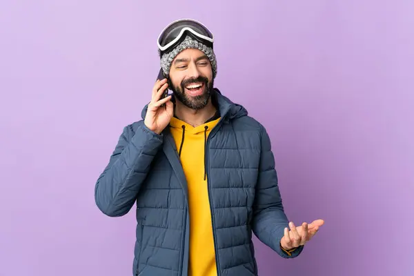 誰かと携帯電話との会話を保つ孤立した紫色の背景の上にスノーボードメガネを持つ熟練した男 — ストック写真