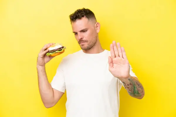 Sarı Arka Planda Izole Edilmiş Hamburgerini Tutan Genç Beyaz Adam — Stok fotoğraf