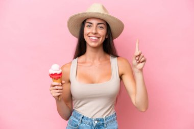 Kornet dondurmalı beyaz bir kadın pembe arka planda izole edilmiş ve en iyinin işareti olarak parmağını kaldırıyor.