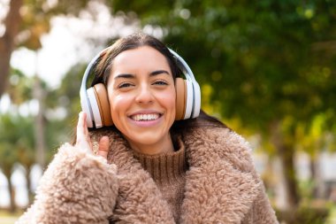Genç esmer kadın açık havada müzik dinliyor.