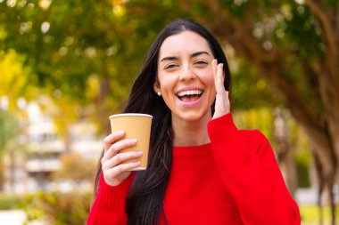 Genç bir kadın açık havada kahvesini yudumlarken ağzı açık bağırıyor.
