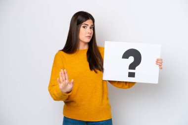 Beyaz arka planda izole edilmiş genç Brezilyalı bir kadın soru işareti yazılı bir levha tutuyor ve dur işareti yapıyor.