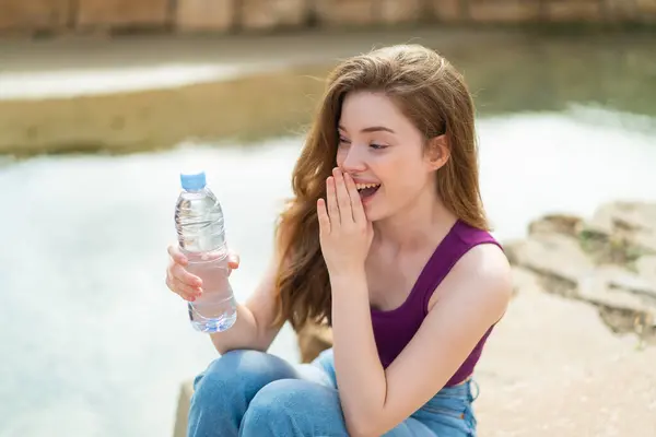 驚きと衝撃的な表情で屋外で水のボトルを持つ若い赤毛の女性 — ストック写真