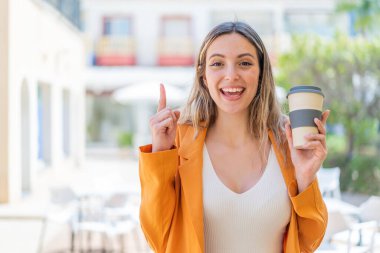 Genç ve güzel bir kadın açık havada kahve alıp harika bir fikre işaret ediyor.