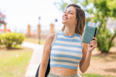Pasaportu elinde tutan güzel bir kadın gülümserken yukarı bakıyor.