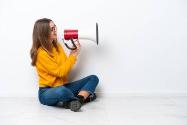 Beyaz arka planda izole bir şekilde yerde oturan beyaz bir kadın megafonla bağırıyor.