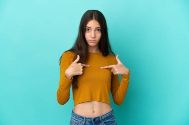 Mavi arka planda izole edilmiş genç bir Fransız kadın kendini işaret ediyor.