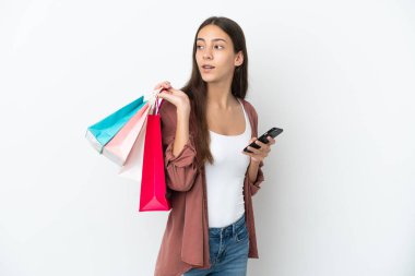 Beyaz arka planda izole edilmiş genç bir Fransız kız elinde alışveriş çantaları ve bir cep telefonu tutuyor.