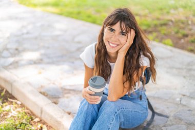 Açık havada elinde kahve tutan genç bir kadın.