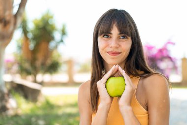 Dışarıda elinde elma tutan genç bir kadın.
