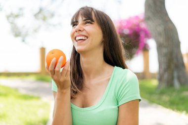 Açık havada elinde mutlu bir ifadeyle bir portakal tutan genç bir kadın.