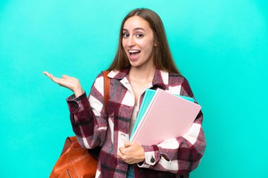 Yüzünde şok ifadesi olan, mavi arka planda izole edilmiş beyaz bir kadın öğrenci.