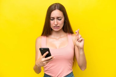 Sarı arka planda izole edilmiş genç beyaz kadın parmakları çapraz cep telefonu kullanıyor.