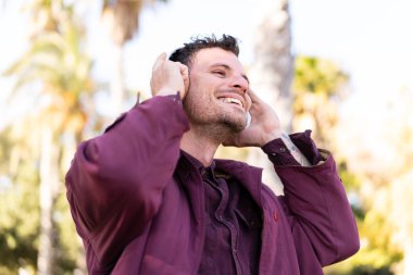 Genç beyaz adam açık havada müzik dinliyor ve şarkı söylüyor.