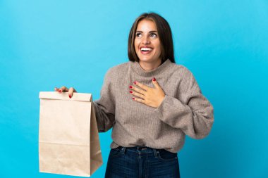 Bir paket yemek alan bir kadın mavi arka planda izole edilmiş bir şekilde gülümsüyor.