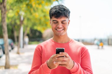 Dışarıdaki İspanyol genç adam cep telefonuyla mesaj ya da e-posta yolluyor.