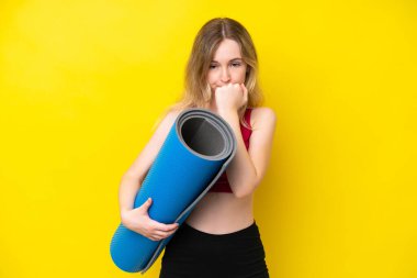 Young sport caucasian woman going to yoga classes while holding a mat isolated on yellow background having doubts