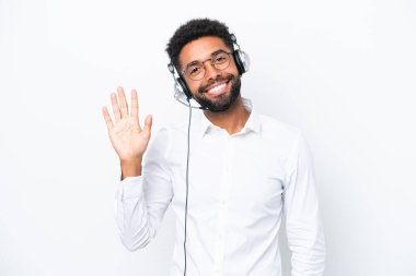 Telemarketer Brazilian man working with a headset isolated on white background saluting with hand with happy expression