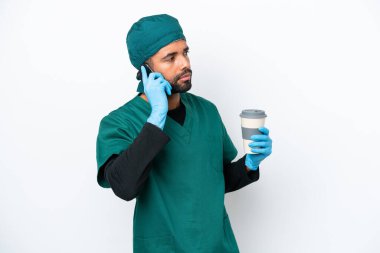 Cerrah Brezilyalı yeşil üniformalı adam beyaz arka planda izole edilmiş. Elinde kahve ve cep telefonu var.