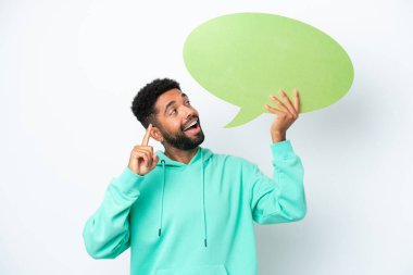 Beyaz arka planda izole edilmiş genç Brezilyalı bir adam boş bir konuşma balonu tutuyor ve düşünüyor.