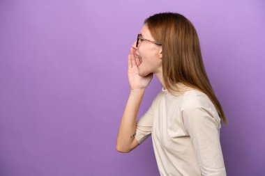 Mor arka planda izole edilmiş genç bir İngiliz kadın ağzı sonuna kadar açık bağırıyor.