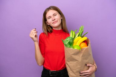 Mor arka planda izole edilmiş alışveriş torbası tutan genç İngiliz kadın para hareketi yapıyor.