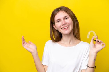 Görünmez diş tellerini tutan genç İngiliz kadın davet etmek için ellerini yana uzatıyor.