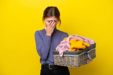 Sarı arka planda, yorgun ve hasta bir ifadeyle izole edilmiş çamaşır sepetini tutan genç İngiliz kadın.