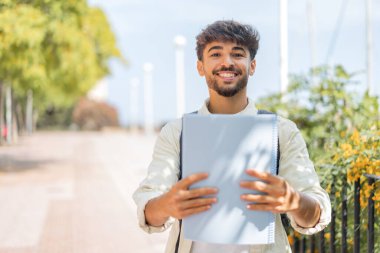 Genç bir Arap öğrenci açık havada neşeli bir ifadeyle.
