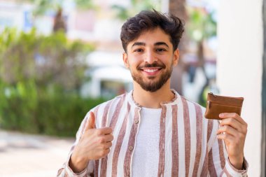 Yakışıklı bir Arap 'ın dışarıda cüzdanı var. Başparmakları havada. Çünkü iyi bir şey oldu.