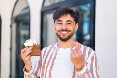 Dışarıdaki yakışıklı Arap, para dolu cüzdanı elinde tutuyor.