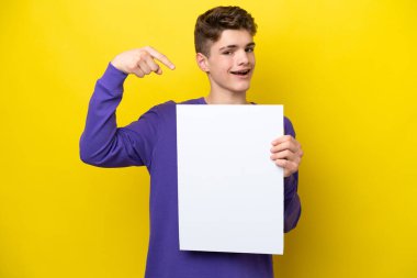 Genç Rus adam sarı arka planda izole edilmiş. Elinde mutlu bir ifadeyle boş bir levha var.