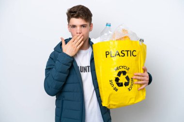 Beyaz arka planda geri dönüşüm için plastik şişelerle dolu bir çanta tutan genç Rus mutlu ve ağzı elle kaplayan bir gülümseme.