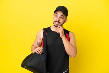 Spor çantalı genç beyaz adam sarı arka planda izole edilmiş bir şekilde yukarı bakarken bir fikir düşünüyor.