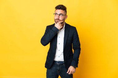 İzole edilmiş sarı arka planda kuşkuları olan ve düşünen bir iş adamı.