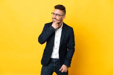 İzole edilmiş sarı arka planda iş adamı yana bakıyor ve gülümsüyor.