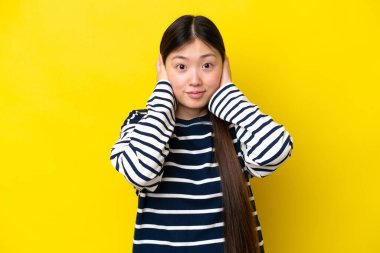 Young Chinese woman isolated on yellow background frustrated and covering ears