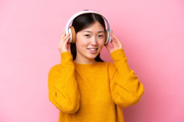 Genç Çinli bir kadın pembe arka planda izole edilmiş müzik dinliyor.