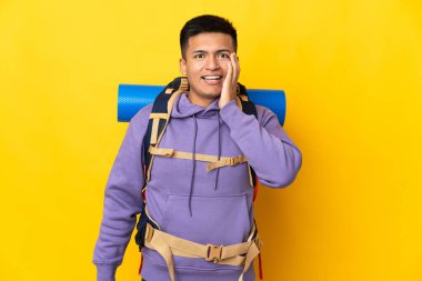 Sarı arka planda büyük bir sırt çantası olan genç dağcı şaşırmış ve şok olmuş yüz ifadesi ile izole edilmiş.