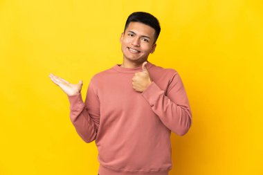 Genç Ekvador 'lu, sarı arka planda izole edilmiş. Kopyalama alanı hayali bir şekilde avucunun içinde duruyor. Bir ilan vermek için.