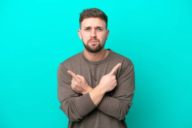 Mavi arka planda izole edilmiş genç beyaz adam, yan taraftakilerin şüphelerine işaret ediyor.