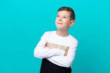 Küçük çocuk mavi arka planda izole edilmiş gülümserken yukarı bakıyor.